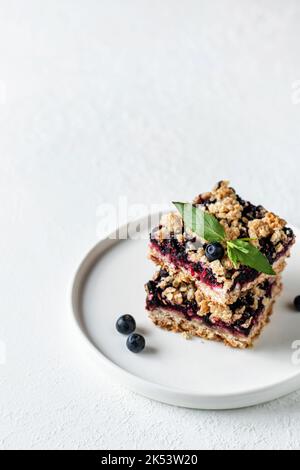 Gebackene Haferflocken-Quadrate mit frischer Heidelbeere und Minze lassen auf weißem Hintergrund mit Textraum. Menü, Rezept Stockfoto