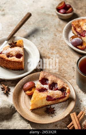 Plum Pie Pieces oder die berühmte Plum Torte der New York Times mit Gewürzen und Tee auf strukturiertem Hintergrund, Rezept im rustikalen Stil Stockfoto