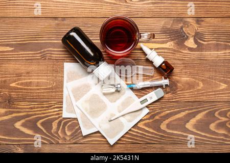 Senfpflaster mit Medikamenten, einer Tasse Tee und einem Thermometer auf Holzgrund Stockfoto