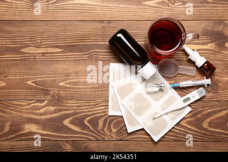 Senfpflaster mit Medikamenten, einer Tasse Tee und einem Thermometer auf Holzgrund Stockfoto