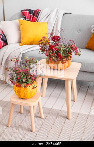 Kürbisse mit schönen Herbstblumen auf Hockern im Wohnzimmer Stockfoto