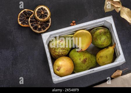 Heller Holzbehälter mit Birnen verschiedener Arten auf schwarzem Herbsthintergrund Stockfoto