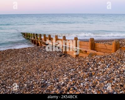 Worthing Beach hölzerner Wellenbrecher führt ins Meer über steinigen Strand bei Sonnenaufgang Großbritannien. Stockfoto