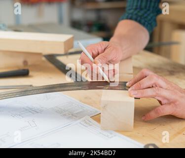 Ein Zimmermann mißt Holzbohlen und macht in einer Werkstatt mit einem Bleistift Markierungen. Stockfoto