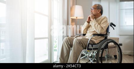 Einsam älter nachdenklicher trauriger alter Mann schaut draußen vor den Fenstern im Schlafzimmer im Altersheim, asiatischer älterer Mann behindert fühlt sich deprimiert einsam allein sitzend Stockfoto