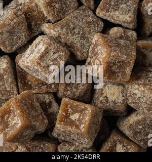 Stapel von gezackten Stücken, goldbraunes würfelförmiges, unraffiniertes Zuckerprodukt, auch als kithul-gezacktes oder Palmzucker bezeichnet, Hintergrund im Vollformat Stockfoto