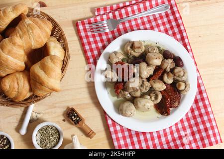 Pilze, sonnengetrocknete Tomaten, Oliven und Kapern in Olivenöl auf rustikalem Holztisch Stockfoto