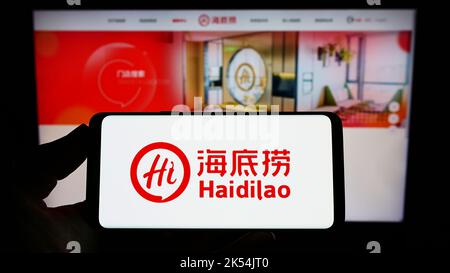 Person, die das Smartphone mit dem Logo der Firma Haidilao International Holding Ltd. Auf dem Bildschirm vor der Website hält. Konzentrieren Sie sich auf die Telefonanzeige. Stockfoto