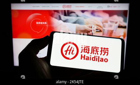 Person, die Mobiltelefon mit Logo der Firma Haidilao International Holding Ltd. Auf dem Bildschirm vor der Business-Webseite hält. Konzentrieren Sie sich auf die Telefonanzeige. Stockfoto