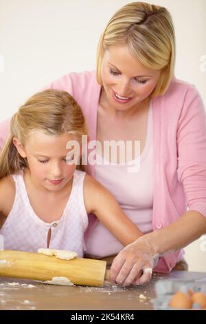 Backen lernen - Perfektionieren ihrer Technik. Eine Mutter hilft ihrer Tochter, den Keksteig auszurollen. Stockfoto