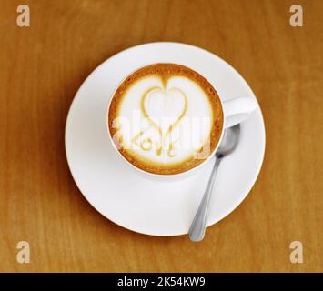 Hergestellt mit liebevollen Händen...Hochwinkelaufnahme einer liebevoll zubereiteten Tasse Cappuccino, die auf einem Kaffeetisch sitzt. Stockfoto