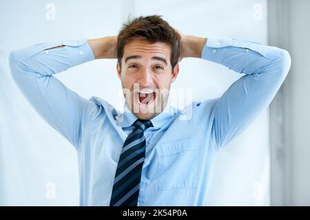 Er verliert seinen Verstand am Arbeitsplatz. Porträt eines jungen Geschäftsmannes, der mit den Händen hinter dem Kopf schreit. Stockfoto