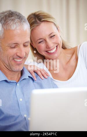 E-Mails werden abgerufen. Ein Ehepaar sitzt mit seinem Laptop und lächelt glücklich. Stockfoto