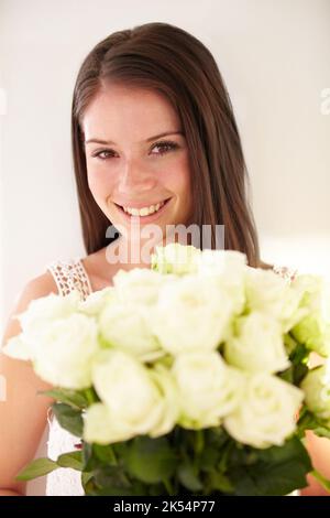 Shes a lovely wie die Rosen, die sie hält. Porträt einer schönen jungen Frau, die lächelt und einen Blumenstrauß hält. Stockfoto