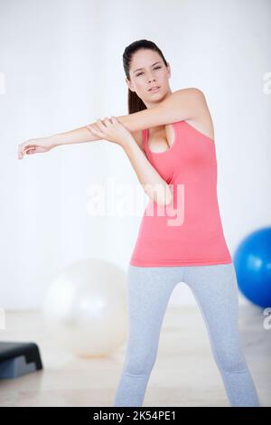 Vorbereitung auf das Fitnessstudio. Junge Frau macht Dehnübungen, während sie im Fitnessstudio steht. Stockfoto