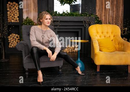 Schöne Frau mit Make-up und Frisur posiert zu Hause in einem dunklen Wohnzimmer in der Nähe eines Kamin für weihnachten dekoriert Stockfoto