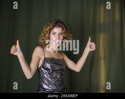 Portrait von attraktiven coquettish lustig fröhlich Mädchen 18 Jahre mit lockigem Haar zeigt wie mit Fingern. Freude, gute Empfehlung, Erfolg, Sieg, Stockfoto