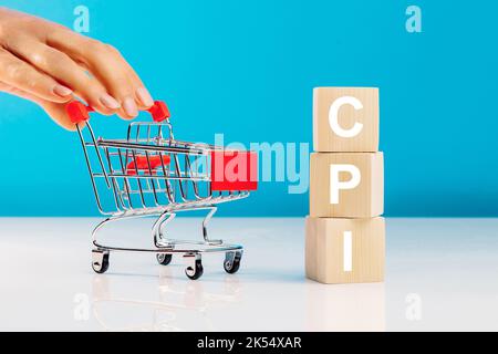 CPI - Verbraucherpreisindex-Symbol.Buchstabenblock im Wort CPI Abkürzung für Verbraucherpreisindex und Frauenhand, die den leeren Warenkorb auf blau drückt b Stockfoto