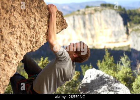 Hoch hängend. Profil eines Felskletterers, der am Rand einer Klippe mit Bergen im Hintergrund baumelt. Stockfoto