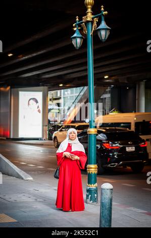 Eine thailändische muslimische Dame steht auf der Sukhumvit Rd, Bangkok, Thailand und benutzt ihr Handy, um ein Foto zu machen. Stockfoto