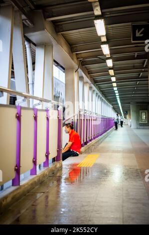 Ein Thailänder sitzt auf den Stufen des Himmelspaziergangs über Bangkoks geschäftigen Straßen. Stockfoto