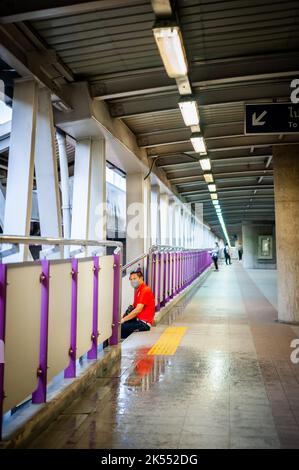 Ein Thailänder sitzt auf den Stufen des Himmelspaziergangs über Bangkoks geschäftigen Straßen. Stockfoto