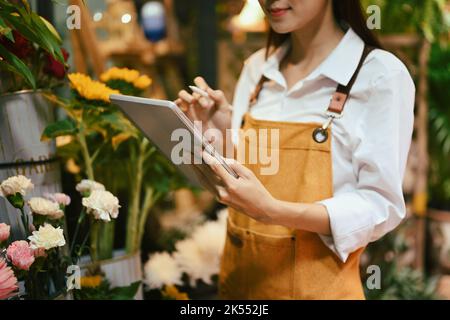 Zugeschnittene Aufnahme von lächelnden weiblichen Floristen Überprüfung, Empfang Online-Bestellung auf digitalem Tablet. Floristik-, Geschäfts- und Technologiekonzept Stockfoto