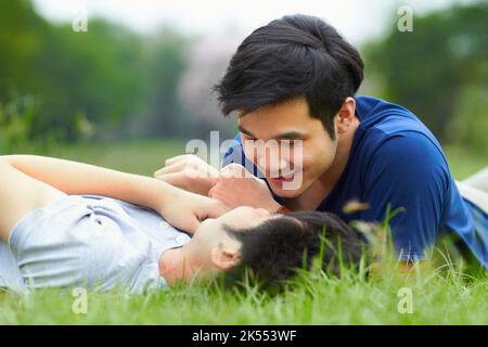 Ein liebevolles junges schwules Paar, das zusammen auf dem Gras liegt. Stockfoto