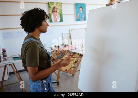 Kunst, Farbe und Maler denken an kreative Idee für Design auf Leinwand während der Arbeit in einem Workshop. Indischer Künstler oder Designer mit Fokus beim Malen Stockfoto