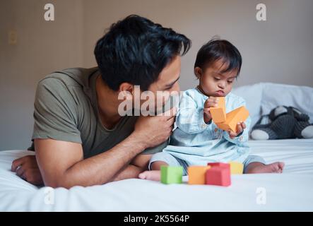 Vater und Down-Syndrom Baby spielen Bildung Spiel mit Spielzeug auf dem Bett für Wachstum und glücklich zusammen. Mann lächelt im Schlafzimmer mit Kleinkind Junge, lernen Stockfoto