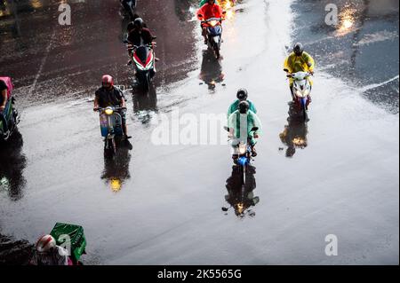 Autos, Minibusse, Busse und Motorräder fahren alle entlang einer belebten Kreuzung an einem regnerischen, dunklen Tag während der Hauptverkehrszeit in Bangkok, Thailand. Stockfoto