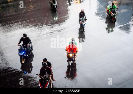 Autos, Minibusse, Busse und Motorräder fahren alle entlang einer belebten Kreuzung an einem regnerischen, dunklen Tag während der Hauptverkehrszeit in Bangkok, Thailand. Stockfoto