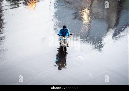 Autos, Minibusse, Busse und Motorräder fahren alle entlang einer belebten Kreuzung an einem regnerischen, dunklen Tag während der Hauptverkehrszeit in Bangkok, Thailand. Stockfoto
