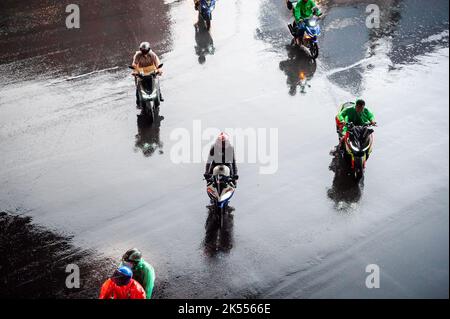 Autos, Minibusse, Busse und Motorräder fahren alle entlang einer belebten Kreuzung an einem regnerischen, dunklen Tag während der Hauptverkehrszeit in Bangkok, Thailand. Stockfoto