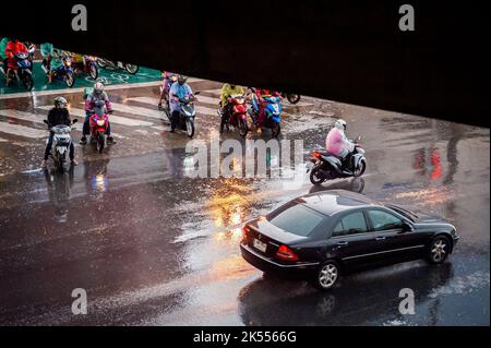 Autos, Minibusse, Busse und Motorräder fahren alle entlang einer belebten Kreuzung an einem regnerischen, dunklen Tag während der Hauptverkehrszeit in Bangkok, Thailand. Stockfoto