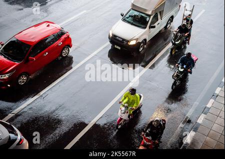 Autos, Minibusse, Busse und Motorräder fahren alle entlang einer belebten Kreuzung an einem regnerischen, dunklen Tag während der Hauptverkehrszeit in Bangkok, Thailand. Stockfoto