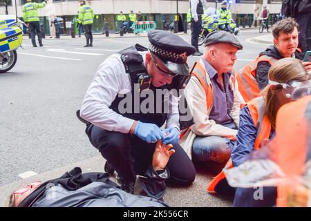 London, Großbritannien. 5.. Oktober 2022. Die Polizei verwendet Lösungsmittel, um den Klebstoff auf den Händen von „Just Stop Oil“-Demonstranten aufzulösen, die die Horseferry Road blockieren. Einige Aktivisten klebten ihre Hände an die Straße, und der Protest war Teil einer Reihe von Demonstrationen, die täglich in Westminster stattfanden, wobei die Klimaschutzgruppe ein Ende der fossilen Brennstoffe und einen Wechsel zu erneuerbaren Energien forderte. Stockfoto