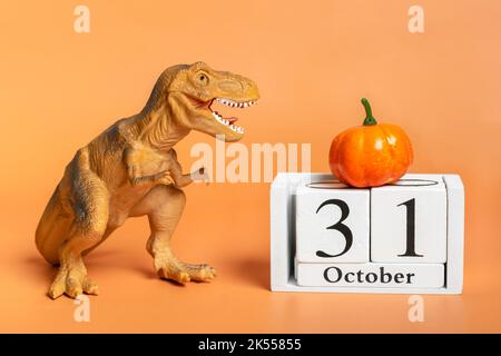 Spielzeug-Dinosaurier Tyrannosaurus Kürbis, Kalenderdatum 31 Oktober isoliert auf orangefarbenem Hintergrund Feiertag Grußkarte Glücklicher Halloween-Tag kreatives Minimalkonzept. Stockfoto