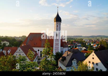 Eine schöne alte Kirche in Burgau mit einem schiefen Turm, umgeben von den alten malerischen Häusern und üppig grünen Bäumen an einem sonnigen Sommertag, Bayern Stockfoto