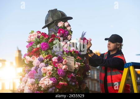 REDAKTIONELLE VERWENDUNG NUR Alice Strutt bringt den letzten Schliff zur Sherlock Holmes Statue, die von Netflix mit einer Blumenverjüngungskur ausgestattet wurde, um die Veröffentlichung ihrer neuesten Fortsetzung 'Enola Holmes 2' vor dem Bahnhof Baker Street in London zu feiern. Bilddatum: Donnerstag, 6. Oktober 2022. Stockfoto