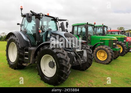 Brydkirk, Schottland - 04. September 2022: Seitenansicht eines Valtra N154 mit zwei John Deere Traktoren im Hintergrund Stockfoto