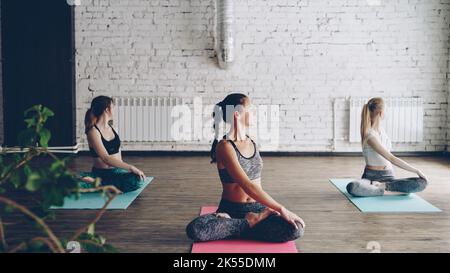 Ziemlich schlanke Mädchen machen Yoga-Übungen unter Anleitung eines erfahrenen Lehrers. Sie beginnen mit Twist Asanas, legen dann die Hände in namaste sitzend in leichter Lotusposition. Stockfoto