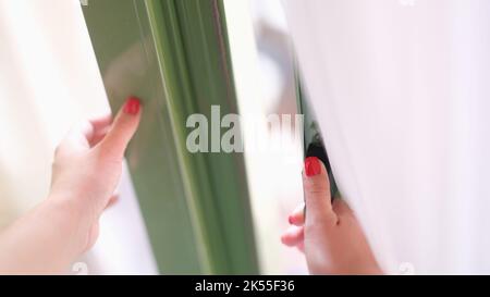 Frau versucht, die Tür zu öffnen, indem sie Fenster oder Türgriff hält Stockfoto