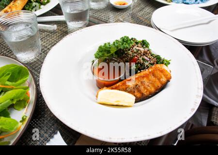 Thai Chef Kochen Essen Fusion-Stil Küche gebraten gegrillt gebratenes Lachssteak gesund mit würziger Sauce und Gemüse Obst Salat auf Keramikplatte pl Stockfoto