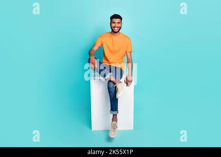 In voller Länge Porträt von fröhlich froh jungen Mann sitzt Podium toothy Lächeln isoliert auf smaragdfarbenen Hintergrund Stockfoto