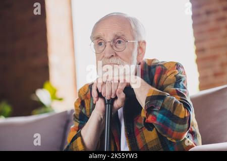 Foto von verärgert deprimiert Opa grau Haar Kopf schlank Gehstock tragen lässig kariert Look Brille sitzen gemütlich Sofa drinnen Wohnzimmer Stockfoto