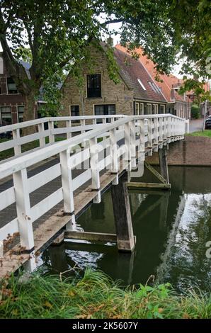 Enkhuizen, Niederlande, 4. Oktober 2022: Blick auf eine schmale hölzerne Fußgängerbrücke über einen Kanal im Stadtteil Boerenhoek Stockfoto