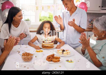 Geburtstag, Kinder und Kuchen mit einem Mädchen bei der Feier mit der Familie auf einer Party, während sie ihre Kerzen ausblasen, um einen Wunsch zu machen. Kinder, Applaus und glücklich Stockfoto