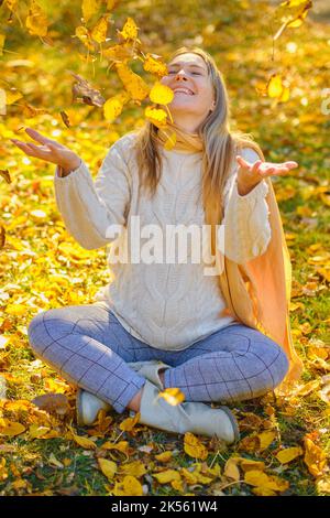 Im Herbst wirft eine junge Frau Blätter in einen Park Stockfoto