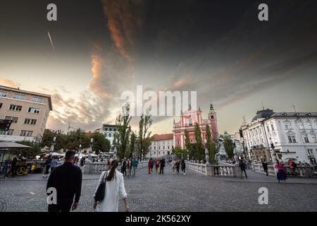 Bild von Menschen, die während eines sonnigen Sommers nach Ljubljana auf der Tromostovje-Brücke (Dreifachbrücke) zwischen dem Presernov-Platz und dem älteren Teil von Ljubljana wandern Stockfoto